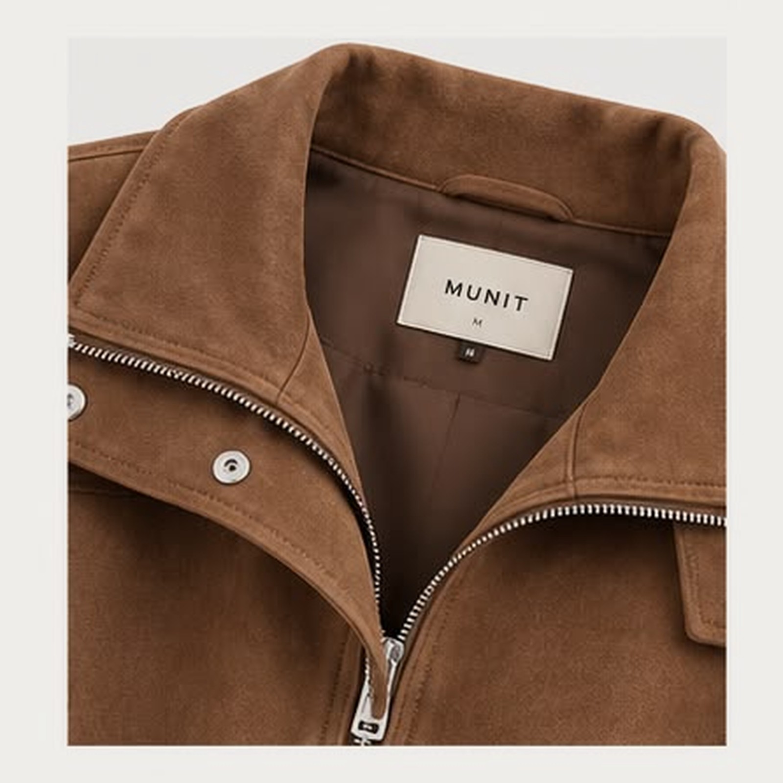 Close view of the collar: two-way zip pull, snapped storm flap tab, and the woven MUNIT label above the lining.