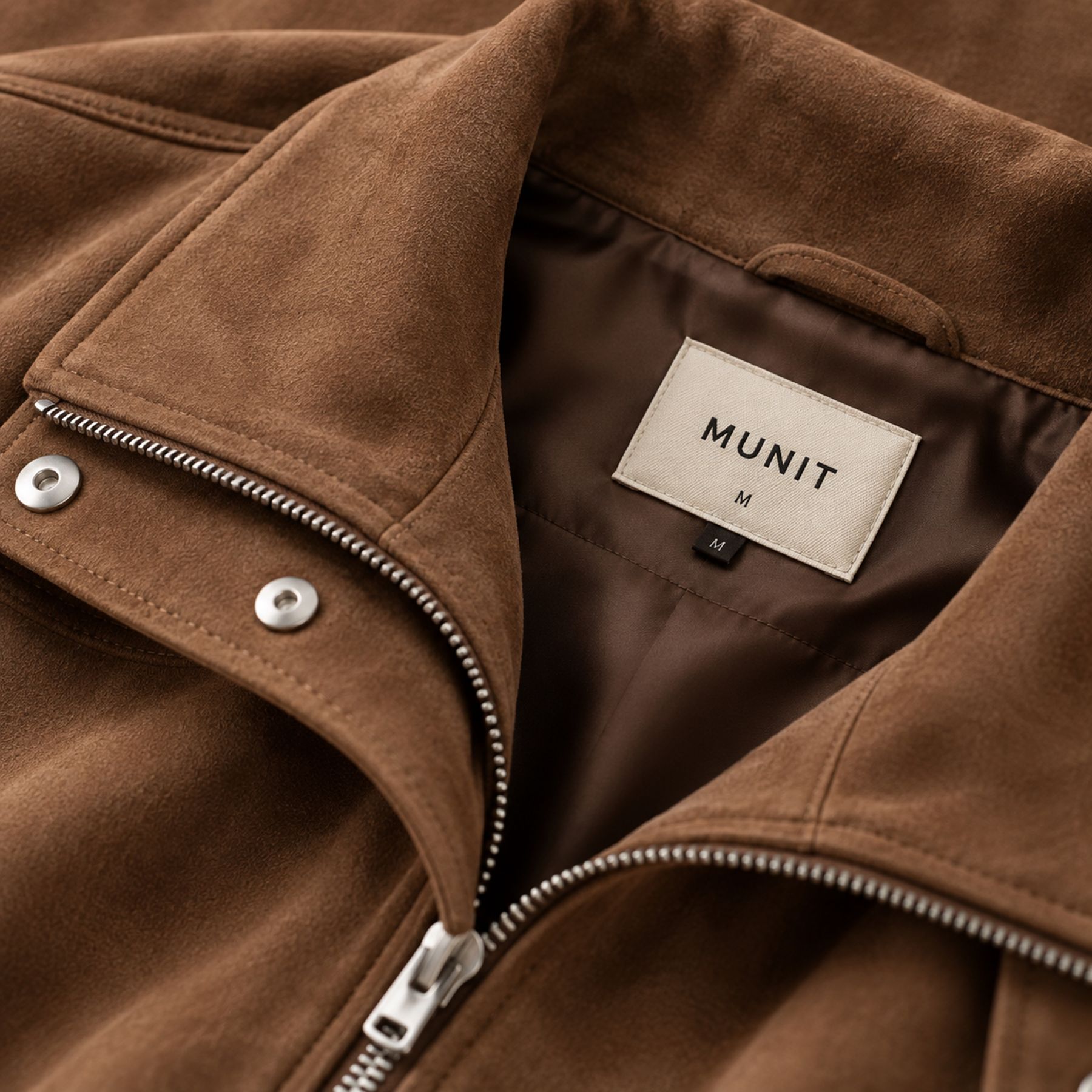 The collar of the brown jacket lying open, with the cream woven MUNIT label and its size letter stitched to the lining.